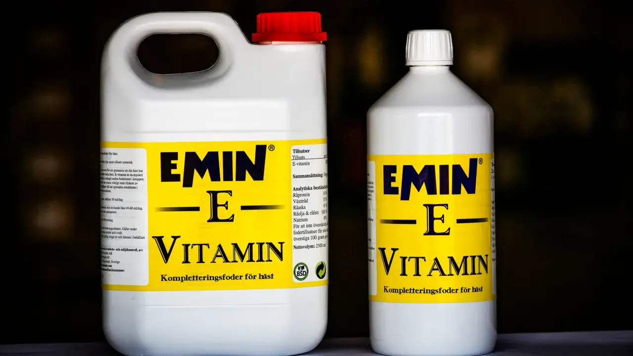 Två flaskor med E-vitamin för hästar. En stor dunk och en mindre flaska, båda med gul etikett och texten "EMIN - E - VITAMIN".