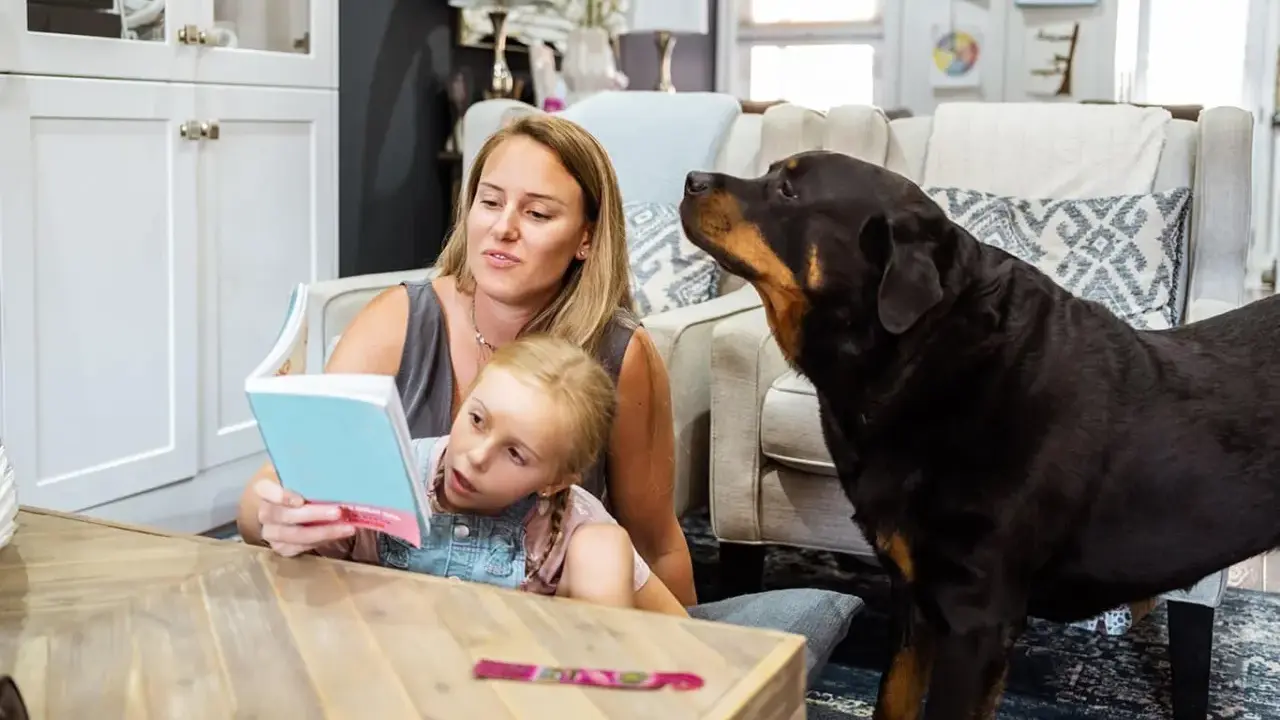 En rottweiler med ett lugnt rottweiler temperament lyssnar uppmärksamt när en mamma läser för sin dotter.
