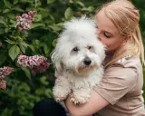 En kvinna kramar sin fluffiga hund. Hundens vita päls är mjuk och fin, och man kan ana den friska huden under.