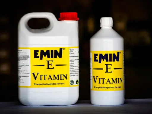 Två flaskor med E-vitamin för hästar. En stor dunk och en mindre flaska, båda med gul etikett och texten "EMIN - E - VITAMIN".