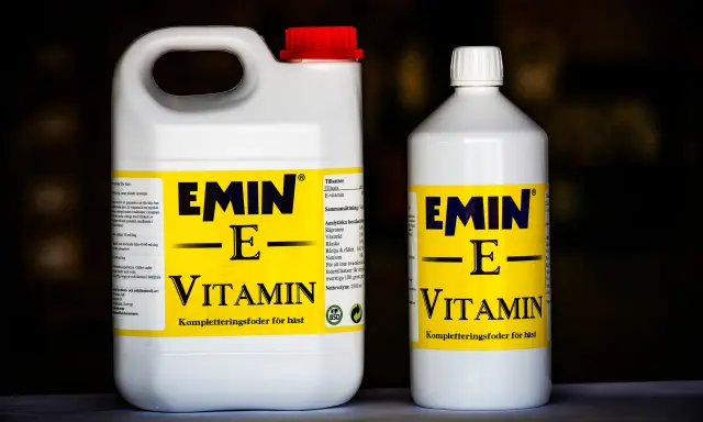 Två flaskor med E-vitamin för hästar. En stor dunk och en mindre flaska, båda med gul etikett och texten "EMIN - E - VITAMIN".