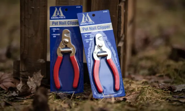 Två förpackningar med Millers klotång, med röda handtag och metallskär, står lutade mot ett trästaket.